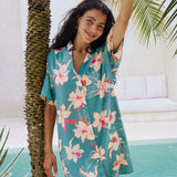 woman with brown hair wearing collared button up dress in teal with large cream colored orchids.