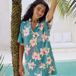 woman with brown hair wearing collared button up dress in teal with large cream colored orchids.