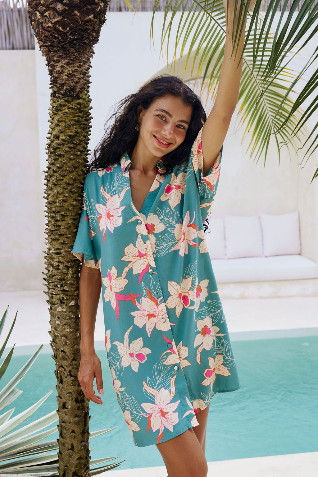 woman with brown hair wearing collared button up dress in teal with large cream colored orchids.