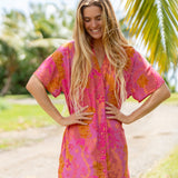 woman wearing a pink v neck button up mini dress with lei print
