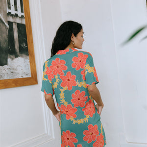 woman with brown hair wearing collared button down dress with orange and yellow lei pua print