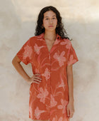 Woman in large floral rust colored short sleeve shirt dress with short sleeves that hits at mid thigh.