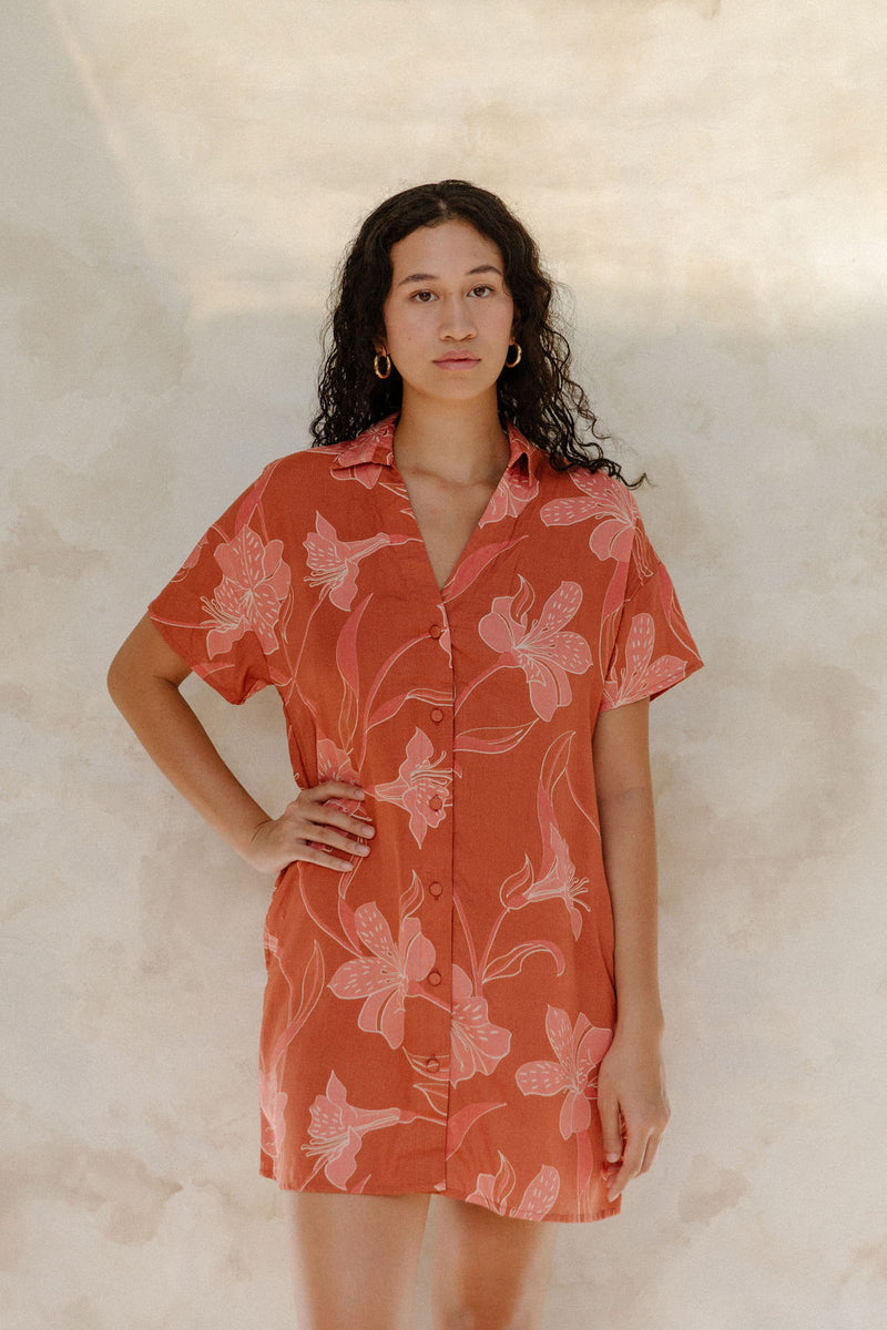 Woman in large floral rust colored short sleeve shirt dress with short sleeves that hits at mid thigh.