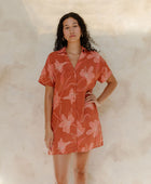 Woman in large floral rust colored short sleeve shirt dress with short sleeves that hits at mid thigh.