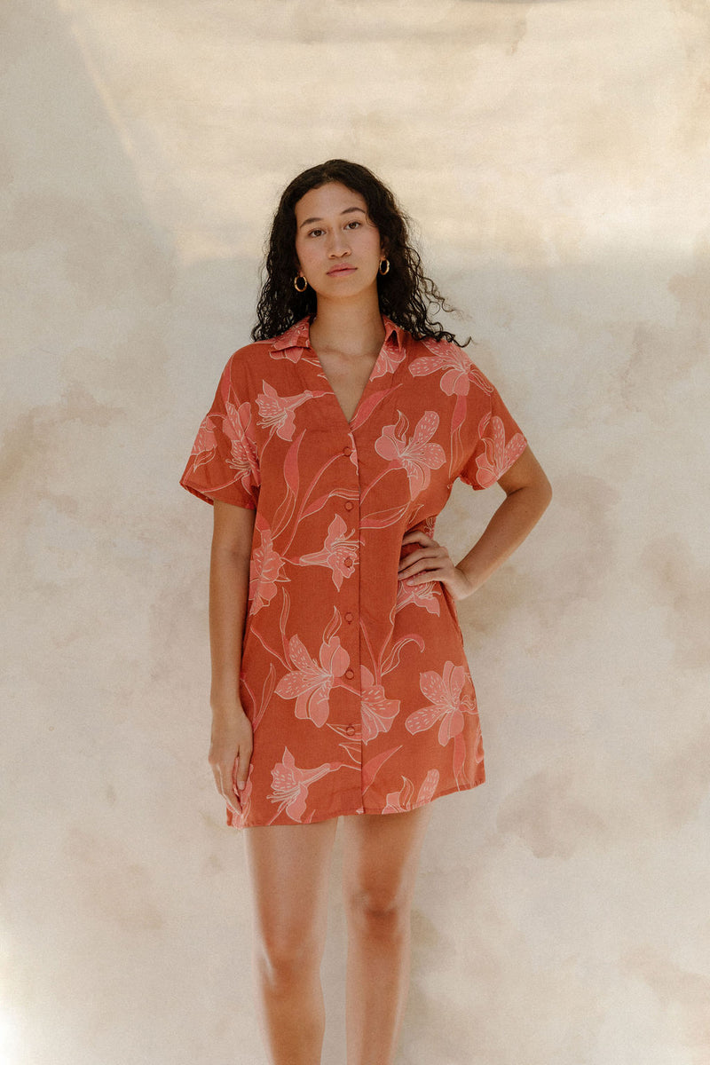 Woman in large floral rust colored short sleeve shirt dress with short sleeves that hits at mid thigh.