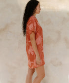 Woman in large floral rust colored short sleeve shirt dress with short sleeves that hits at mid thigh.