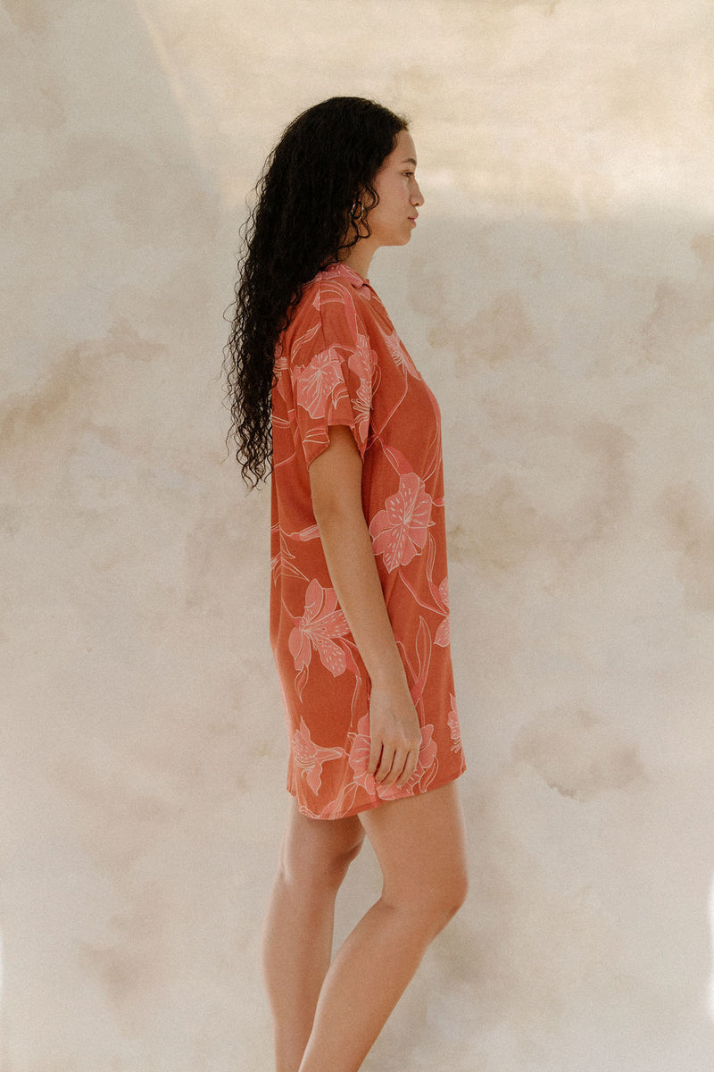 Woman in large floral rust colored short sleeve shirt dress with short sleeves that hits at mid thigh.