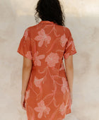 Woman in large floral rust colored short sleeve shirt dress with short sleeves that hits at mid thigh.