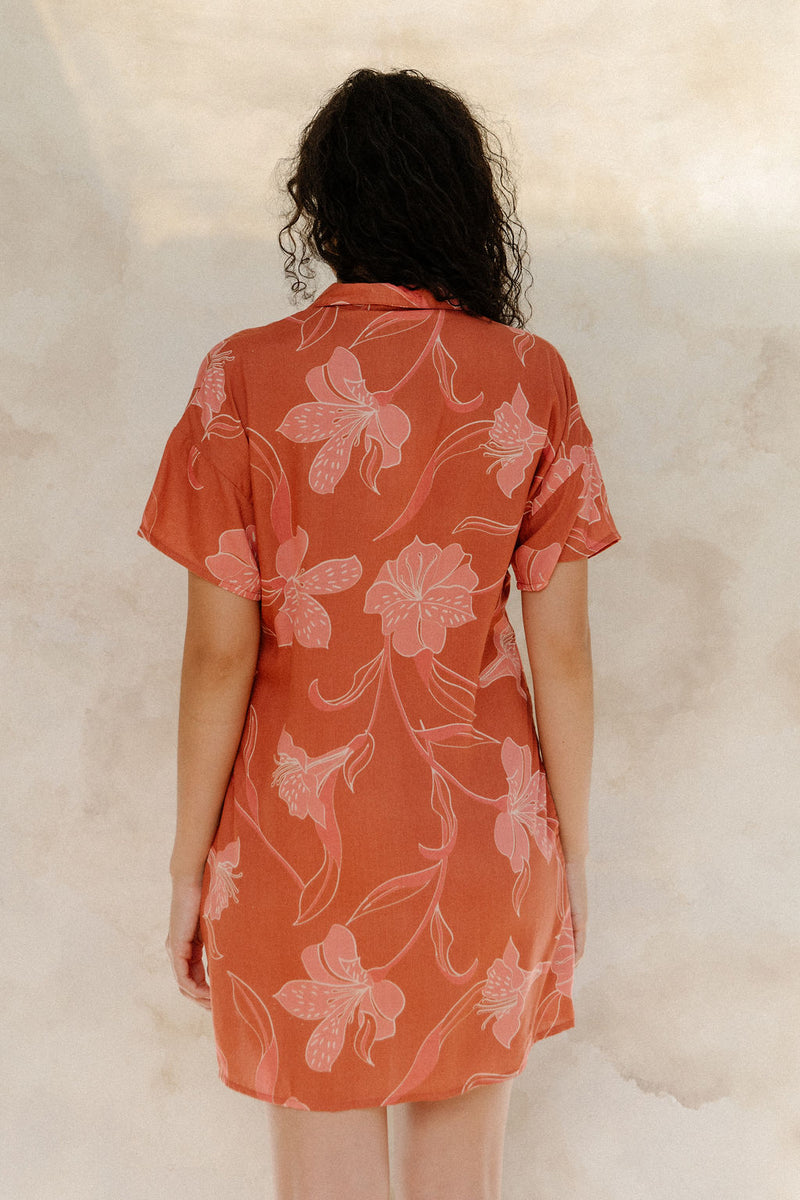 Woman in large floral rust colored short sleeve shirt dress with short sleeves that hits at mid thigh.