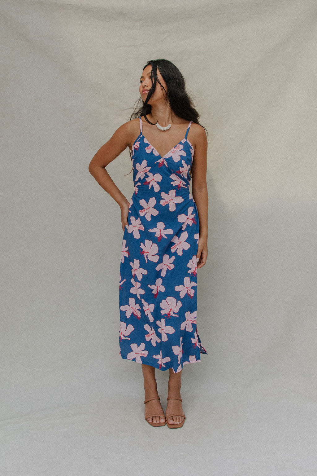 woman with brown hair wearing a navy v neck tie back dress with white hibiscus print