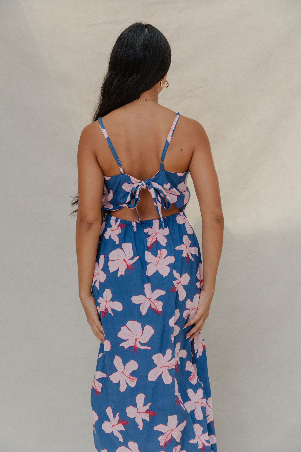 woman with brown hair wearing a navy v neck tie back dress with white hibiscus print