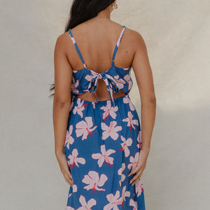 woman with brown hair wearing a navy v neck tie back dress with white hibiscus print