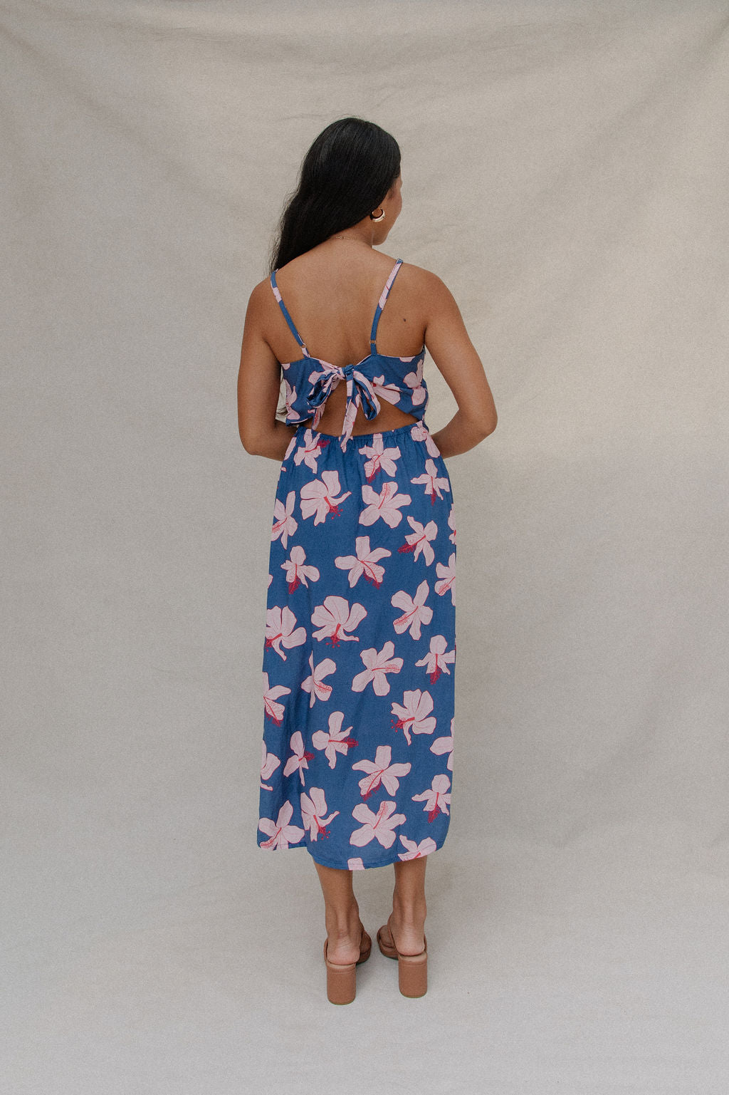 woman with brown hair wearing a navy v neck tie back dress with white hibiscus print