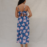 woman with brown hair wearing a navy v neck tie back dress with white hibiscus print