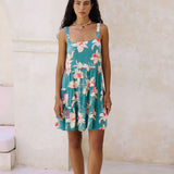 woman with brown hair wearing a tiered mini dress in teal with large cream colored orchids.
