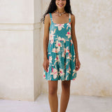woman with brown hair wearing a tiered mini dress in teal with large cream colored orchids.