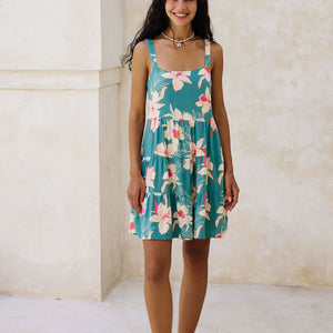 woman with brown hair wearing a tiered mini dress in teal with large cream colored orchids.