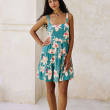 woman with brown hair wearing a tiered mini dress in teal with large cream colored orchids.