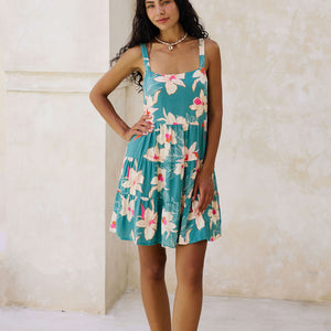 woman with brown hair wearing a tiered mini dress in teal with large cream colored orchids.