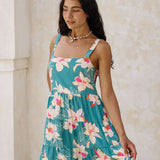woman with brown hair wearing a tiered mini dress in teal with large cream colored orchids.