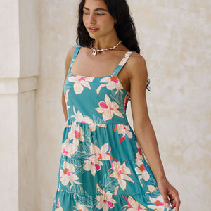 woman with brown hair wearing a tiered mini dress in teal with large cream colored orchids.