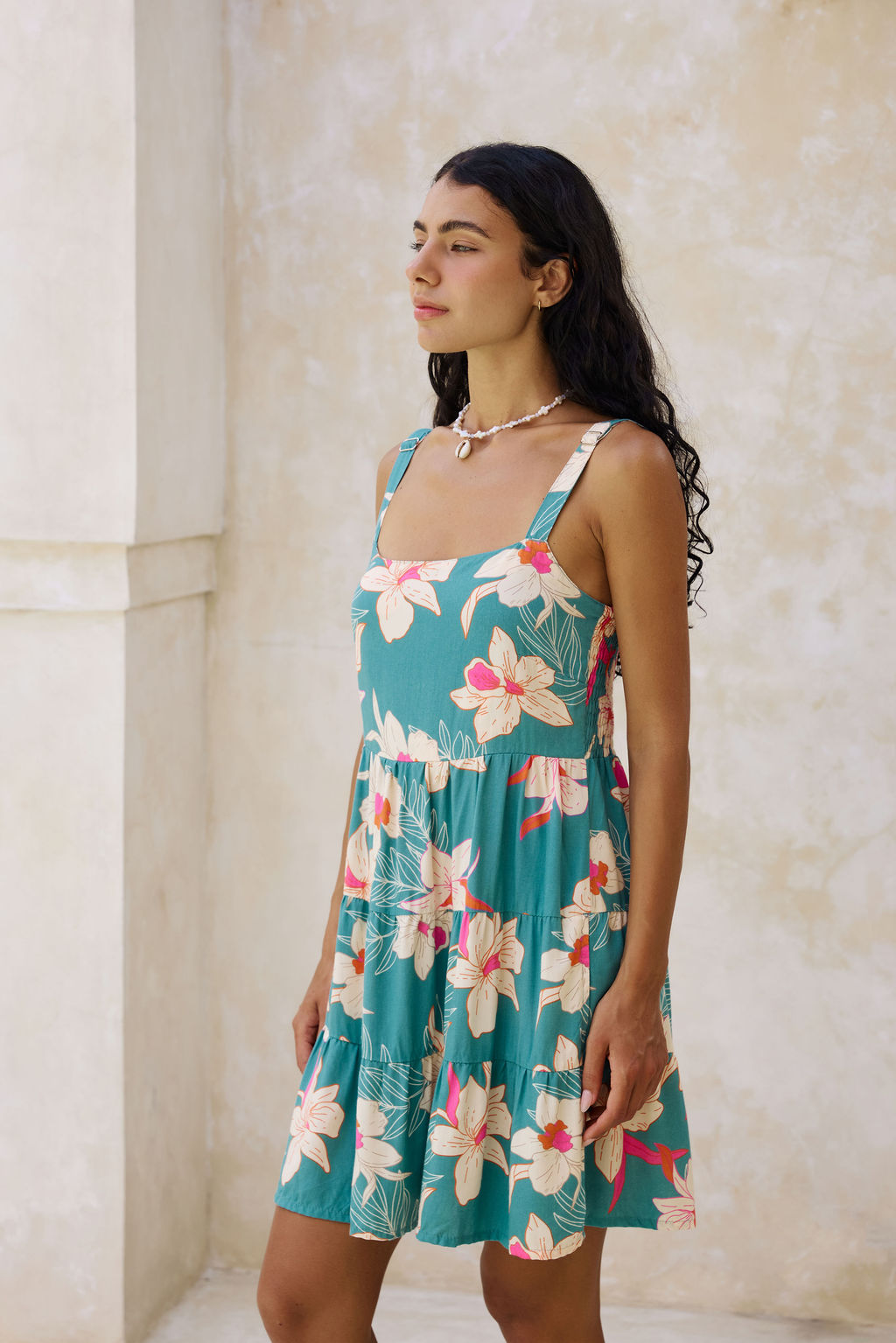  woman with brown hair wearing a tiered mini dress in teal with large cream colored orchids.
