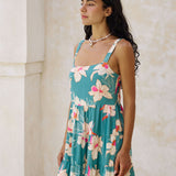  woman with brown hair wearing a tiered mini dress in teal with large cream colored orchids.