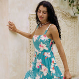 woman with brown hair wearing a tiered mini dress in teal with large cream colored orchids.