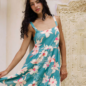 woman with brown hair wearing a tiered mini dress in teal with large cream colored orchids.