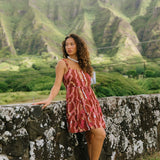 woman with brown hair wearing a red-brown colored mini dress with lei print