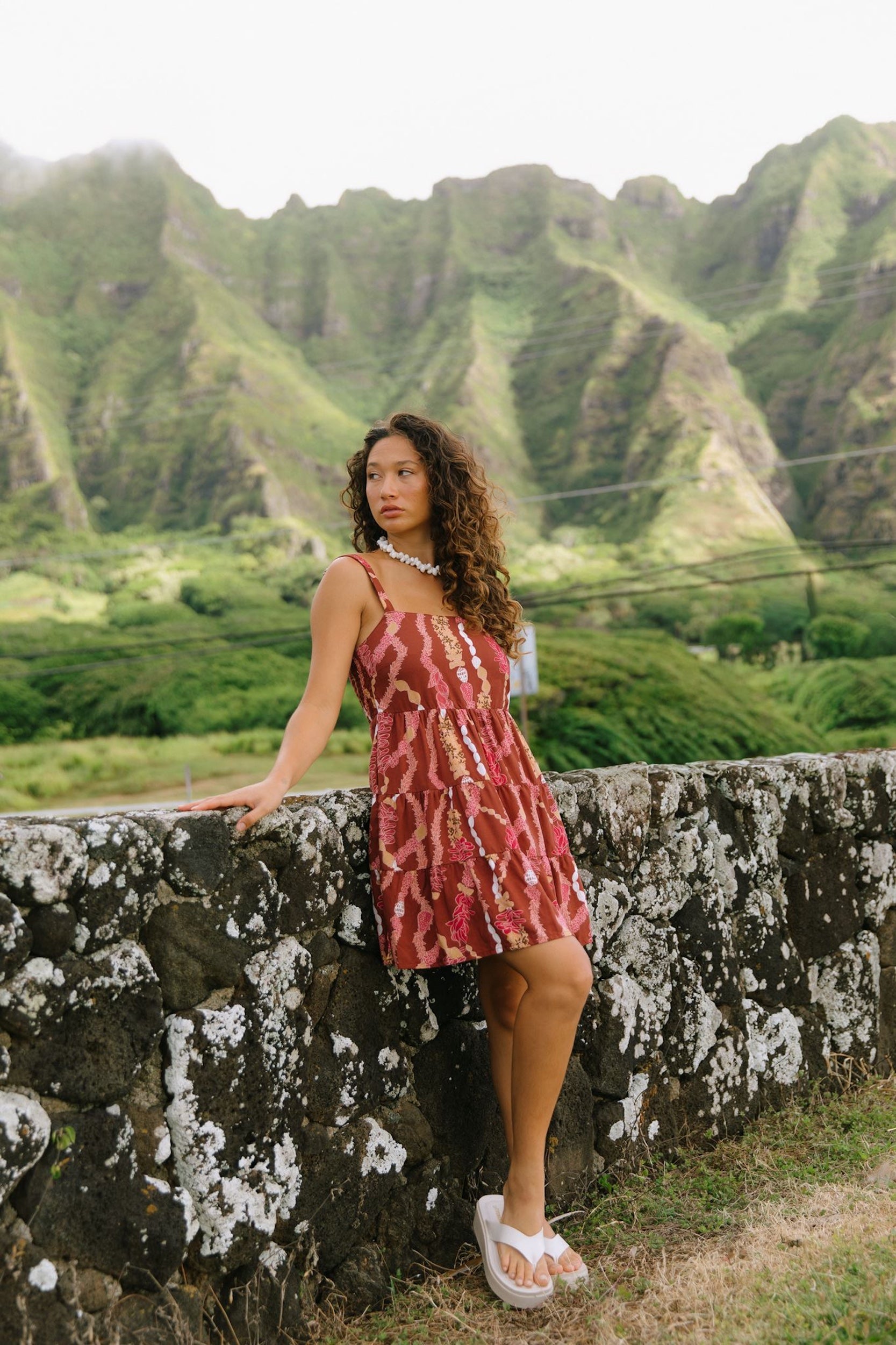 woman with brown hair wearing a red-brown colored mini dress with lei print