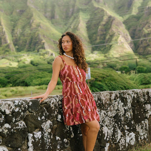 woman with brown hair wearing a red-brown colored mini dress with lei print