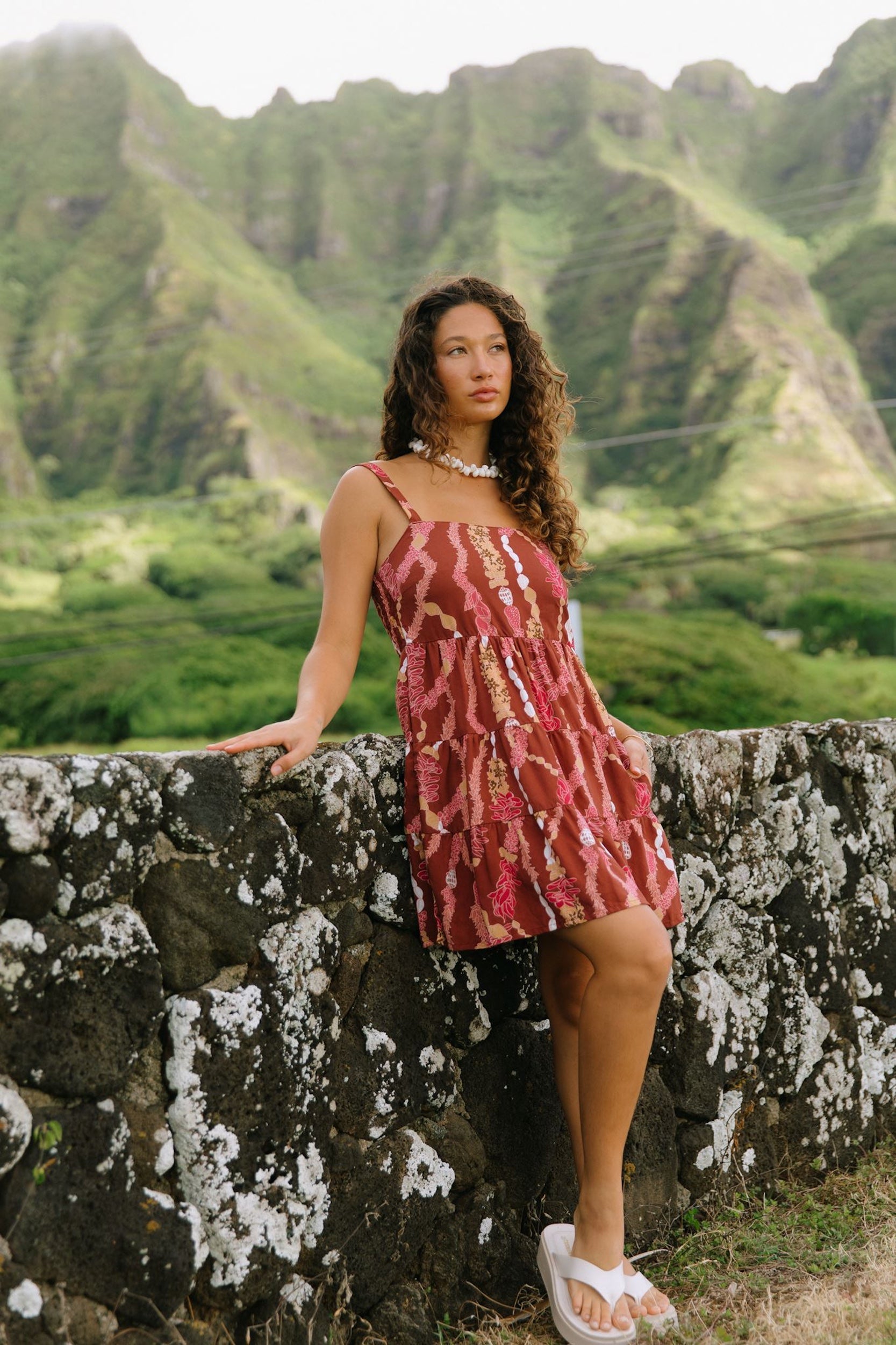 woman with brown hair wearing a red-brown colored mini dress with lei print