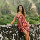 woman with brown hair wearing a red-brown colored mini dress with lei print