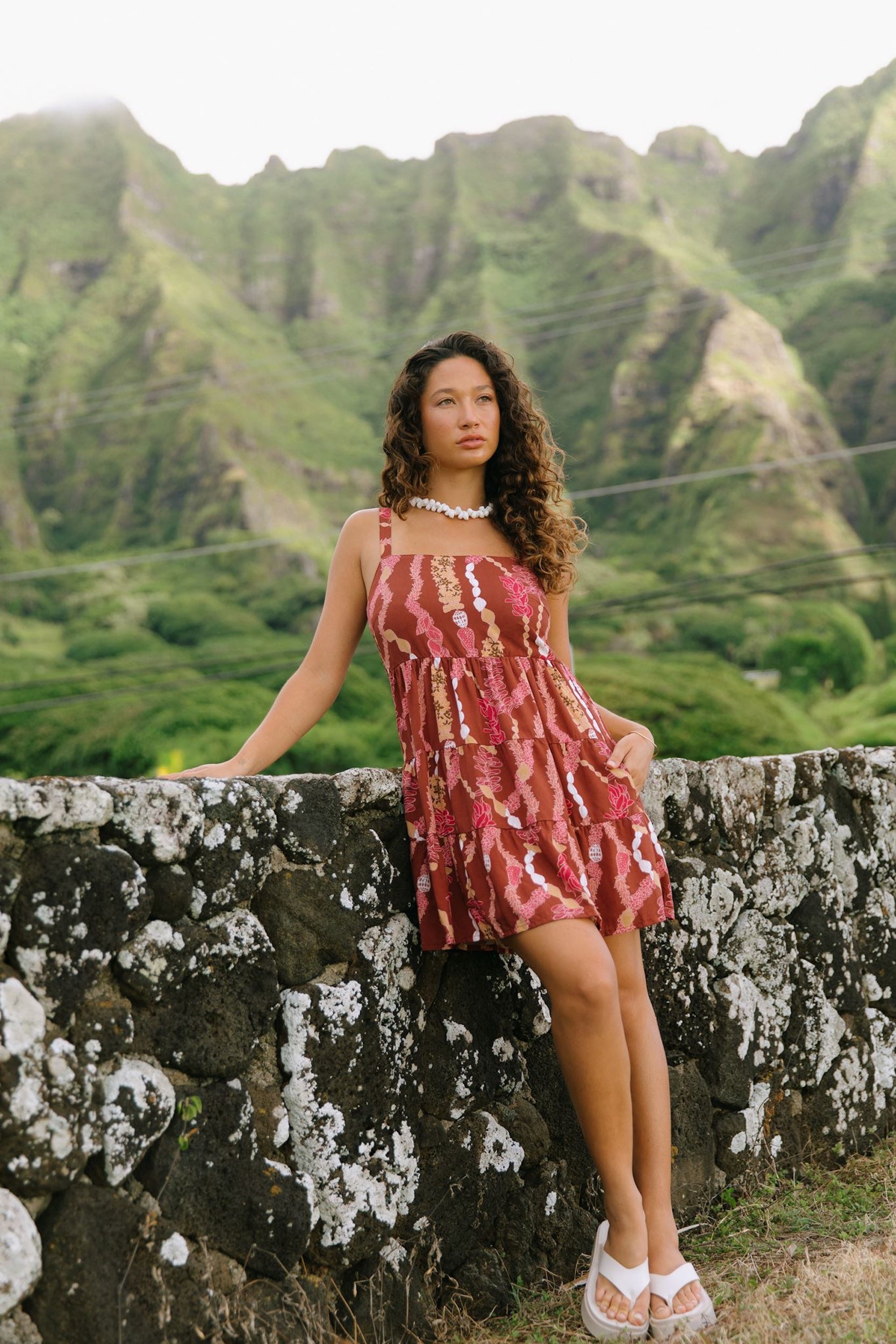 woman with brown hair wearing a red-brown colored mini dress with lei print