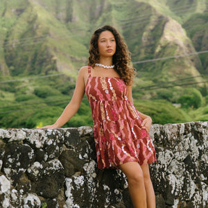 woman with brown hair wearing a red-brown colored mini dress with lei print