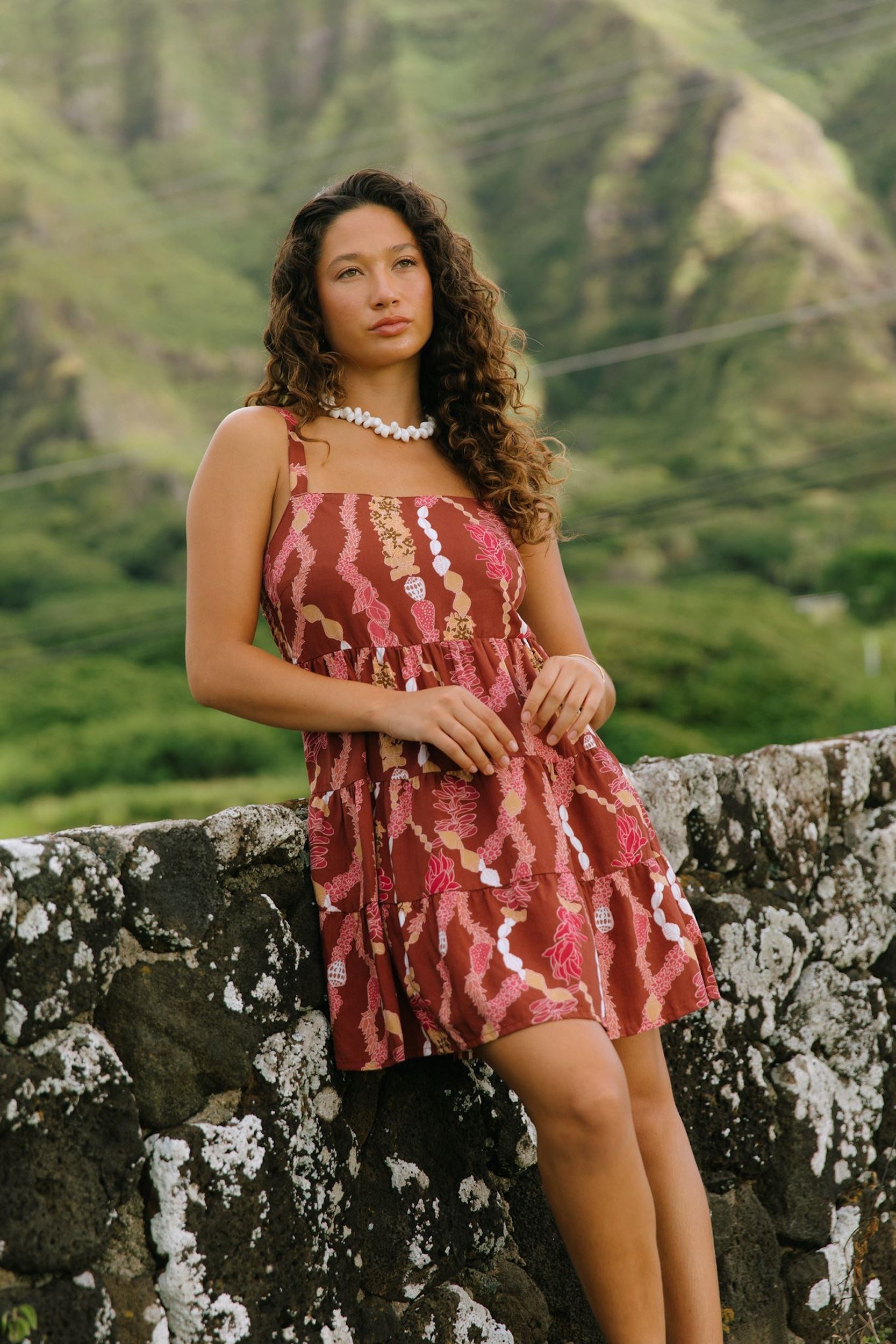 woman with brown hair wearing a red-brown colored mini dress with lei print
