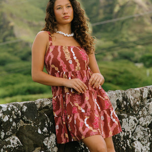 woman with brown hair wearing a red-brown colored mini dress with lei print