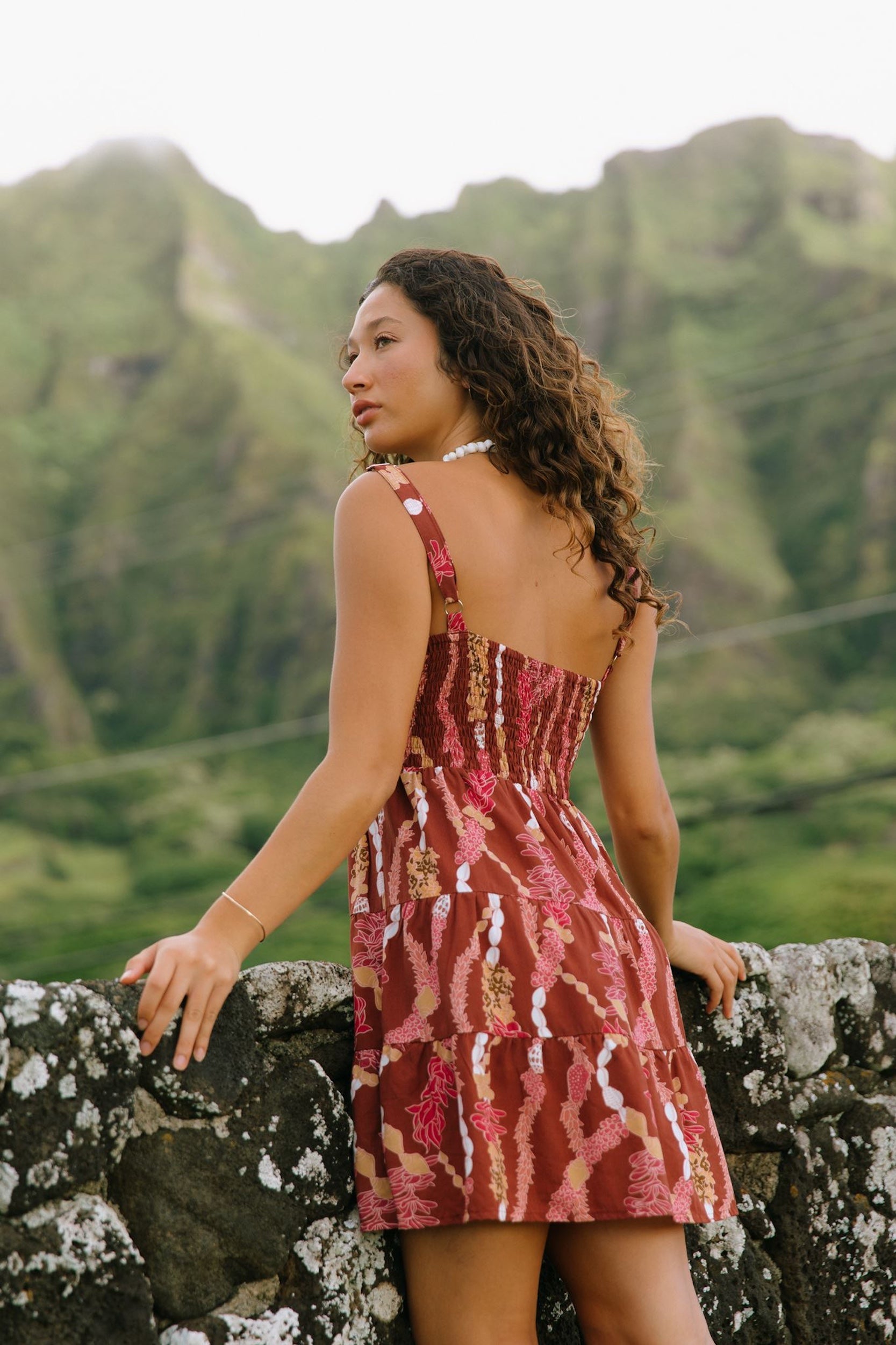 woman with brown hair wearing a red-brown colored mini dress with lei print