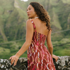 woman with brown hair wearing a red-brown colored mini dress with lei print