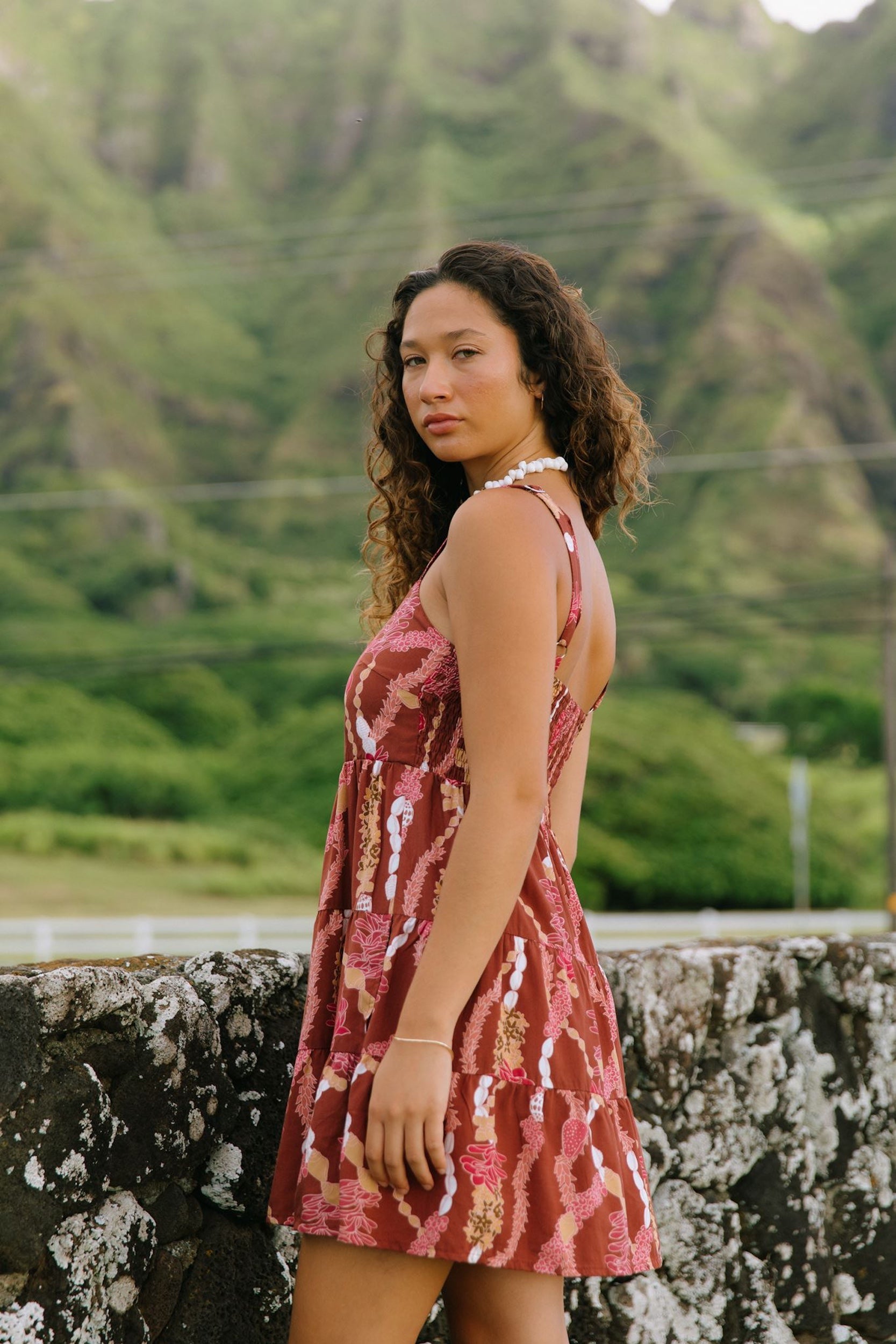 woman with brown hair wearing a red-brown colored mini dress with lei print