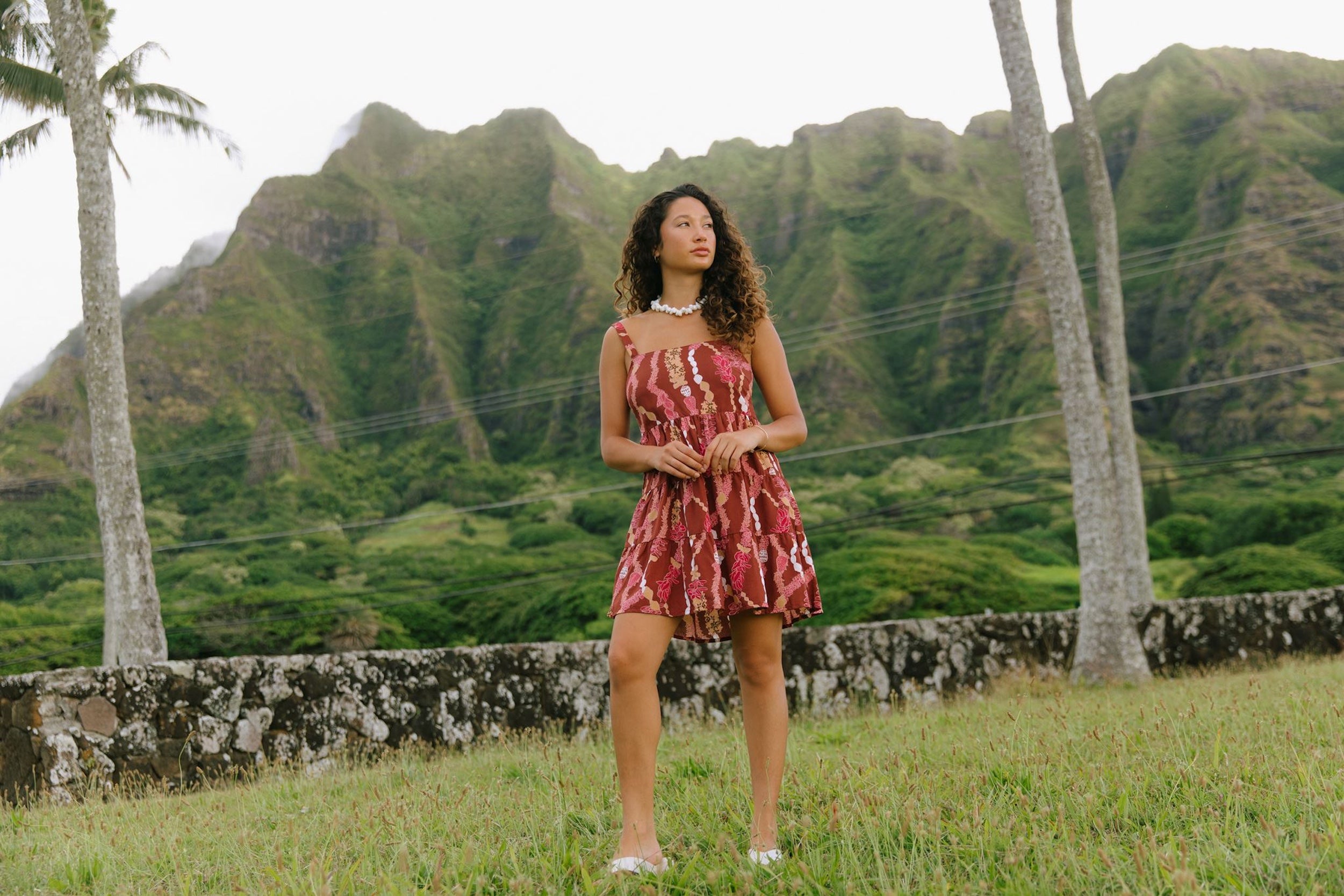 woman with brown hair wearing a red-brown colored mini dress with lei print