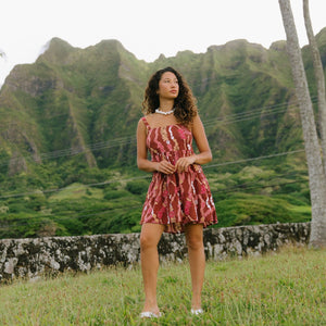 woman with brown hair wearing a red-brown colored mini dress with lei print