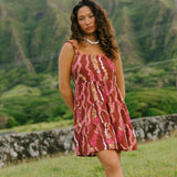 woman with brown hair wearing a red-brown colored mini dress with lei print