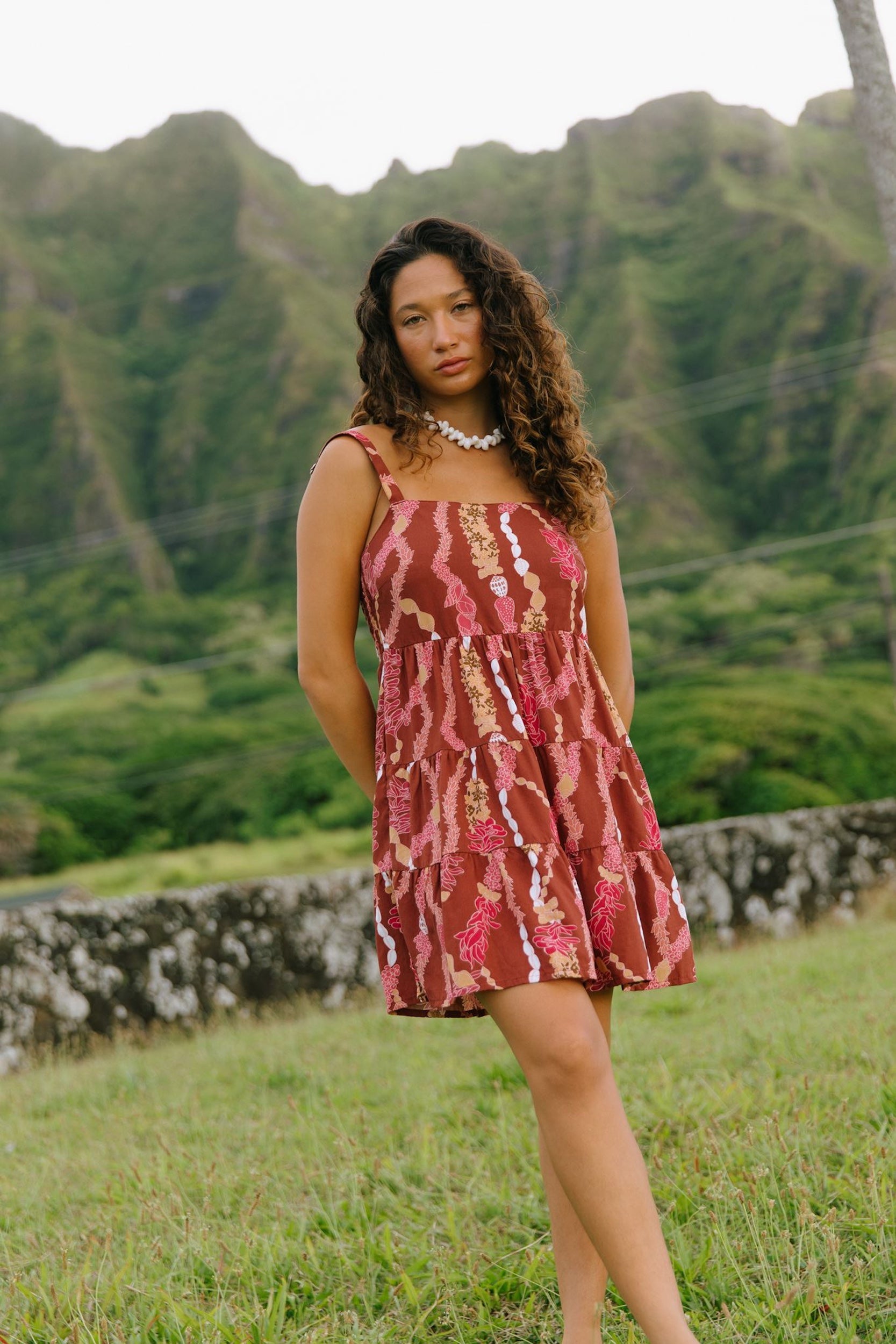 woman with brown hair wearing a red-brown colored mini dress with lei print