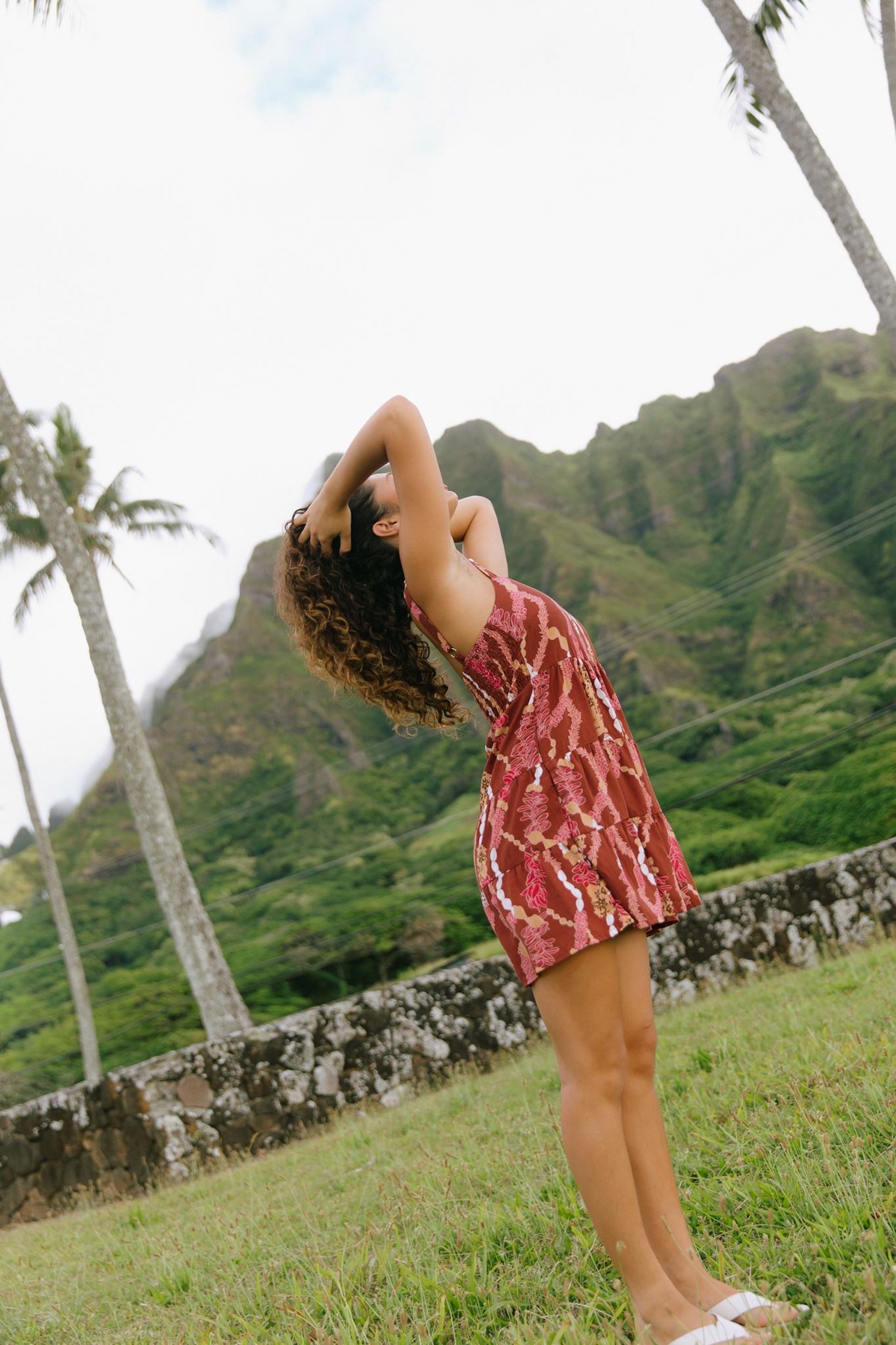woman with brown hair wearing a red-brown colored mini dress with lei print