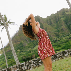 woman with brown hair wearing a red-brown colored mini dress with lei print