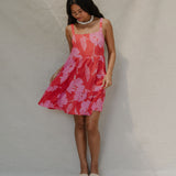 woman with brown hair wearing a red short spaghetti strap dress with pink mao flower pattern