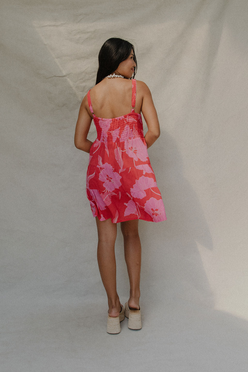 woman with brown hair wearing a red short spaghetti strap dress with pink mao flower pattern