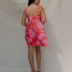 woman with brown hair wearing a red short spaghetti strap dress with pink mao flower pattern